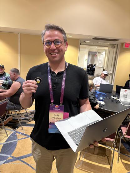 A man holding an open laptop in one hand, and a BeeWare challenge coin in the other.