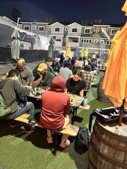 About 15-20 people playing chess outside at a brewery 