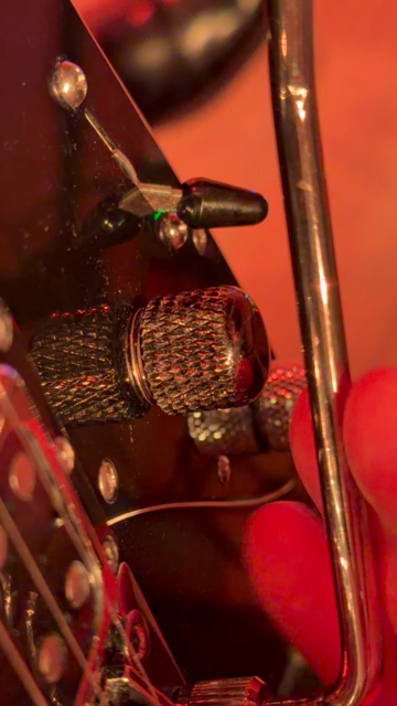 Short video clip looking down from the players point of view at an electric guitar bathed in red stage light, zoomed in on the volume knob, demonstrating the push/push action.