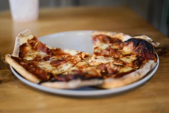 Photograph of a home-made pizza sitting on a raw wooden table. The centre of the pizza is in focus, the near edge and the far edge lost in the depth of field