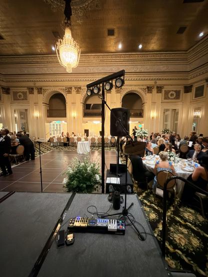 My pedalboard on a stage in a beautiful vintage golden ballroom, dance floor, round tables for wedding guests, head table at the far end of the room.