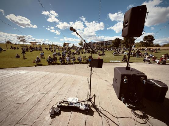 My paddleboard is set up on a concrete stage, with a small PA stack on the right, looking out onto a grassy amphitheatre, under sunny skies and white clouds