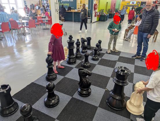 Several children with their faces covered, playing chess with a giant set.