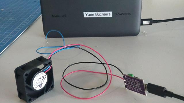 Ein drehender 40mm Lüfter mit Kabeln an einem USB PD board, daran ein USB Kabel an einer Powerbank