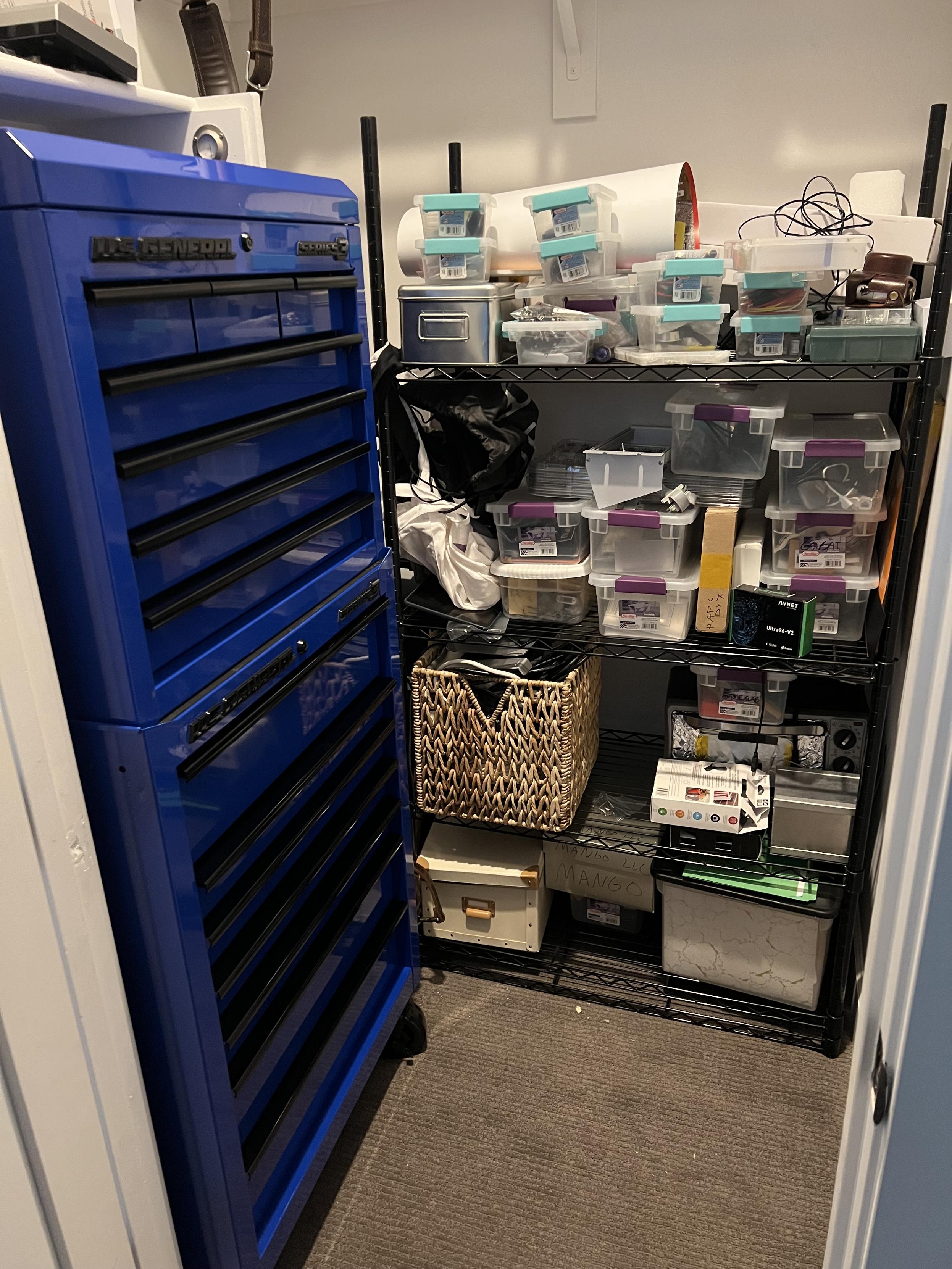 Closet off my office and electronics hobby room with a Harbor Freight toolbox stack (gridfinity inside) and a mesh shelf from Costco with sterilite bins somewhat organized on it and various other boxes and bits, including a toaster oven repurposed for surface mount reflow with a controller box and a wicker bin of cables dating back to the 20th century in case someone needs a null modem cable one day