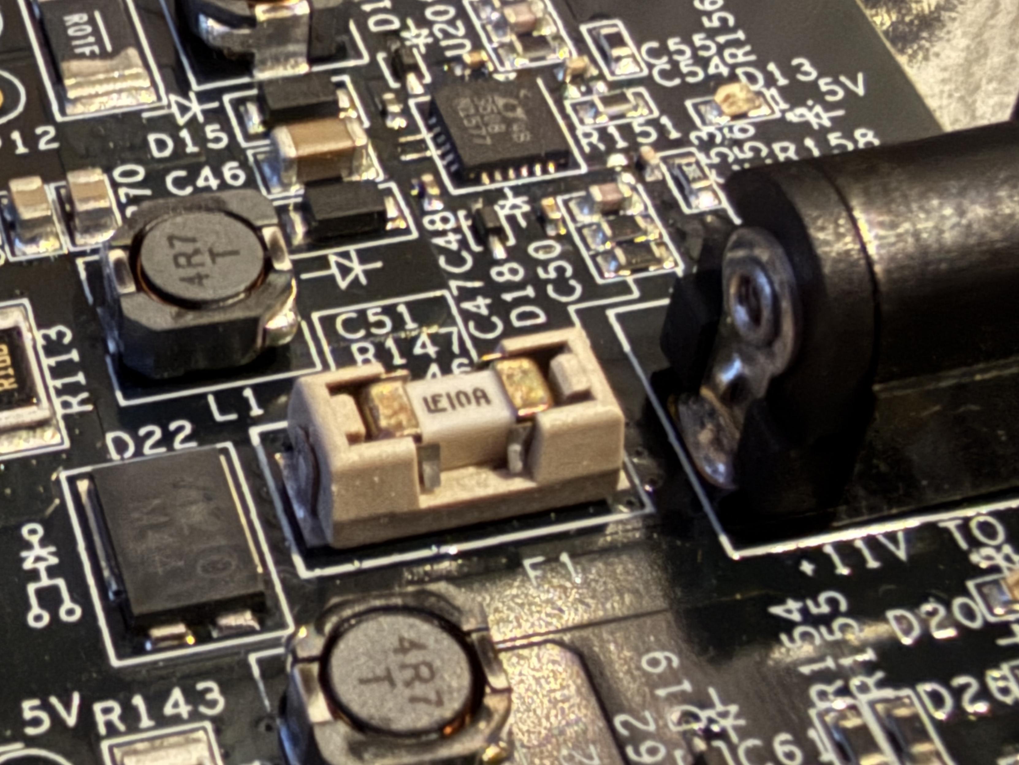 Surface mount socketed fuse near a DC barrel power connector, and two inductors visible above and below along with other passives, a QFN device, and a diode