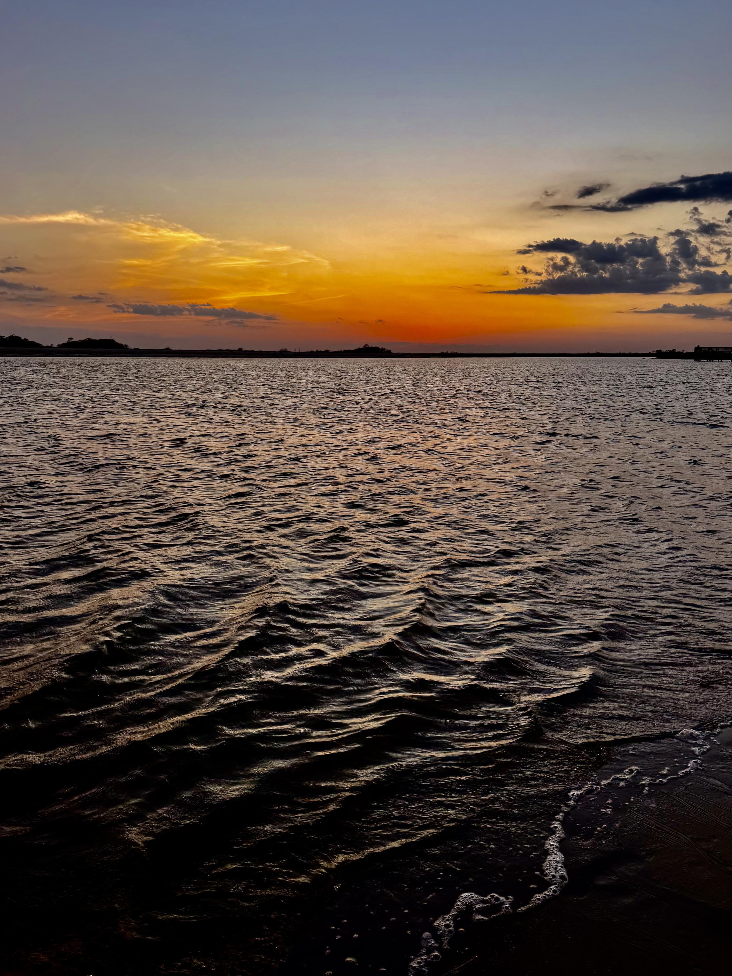 View across an inlet at sunset, waves lapping the shore.