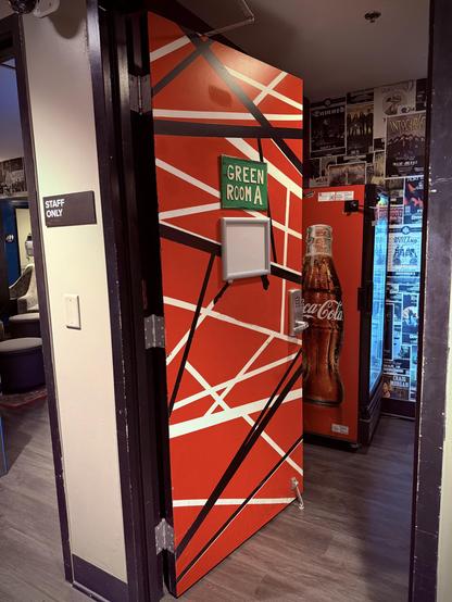 Open orange door labeled "GREEN ROOM A" with Coca-Cola mural; posters on red wall inside.