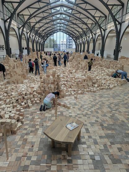 Looking down a hall filled with thousands of wooden blocks and children building all sorts of cool things from them