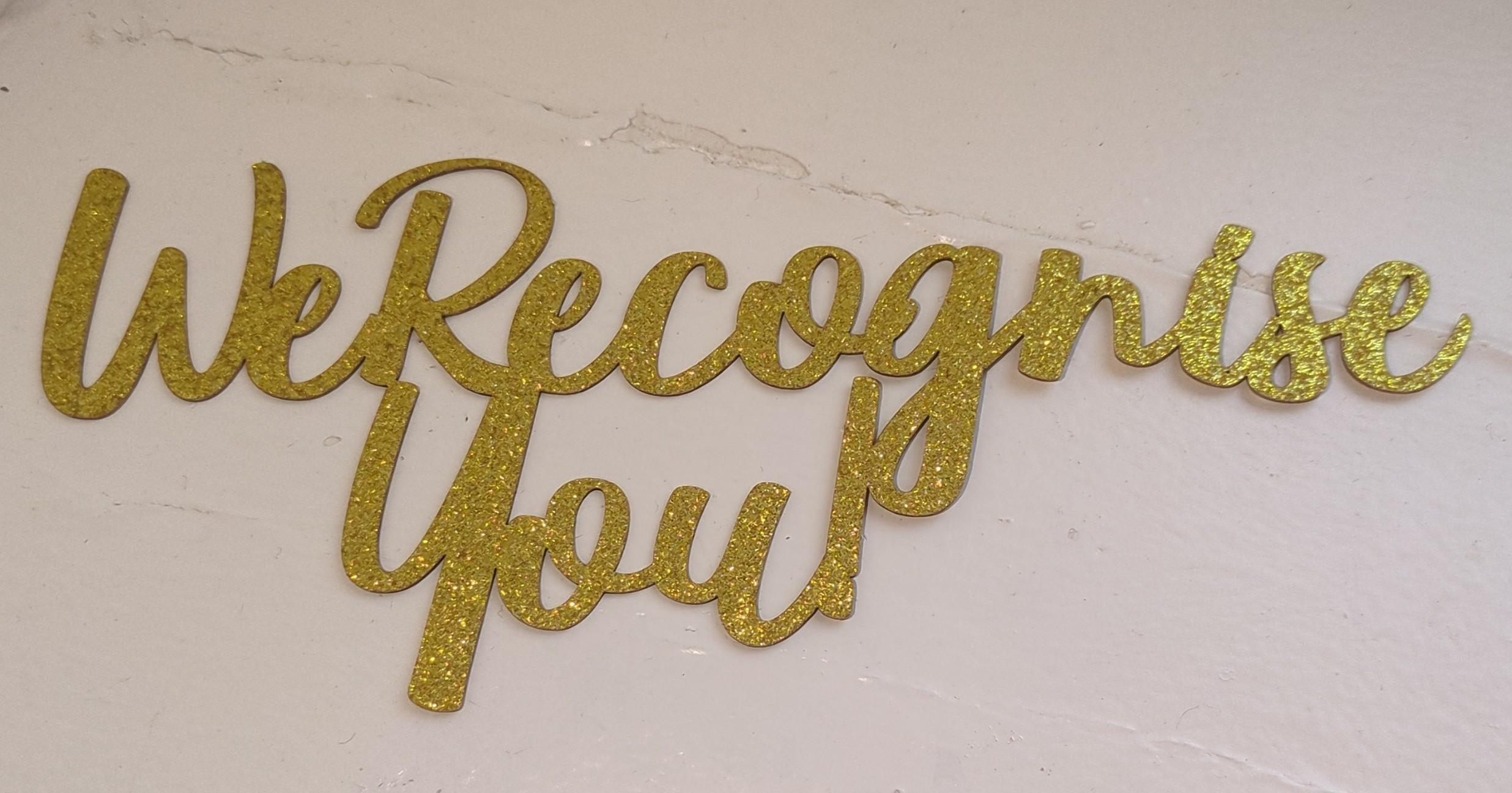 Gold cut out lettering that reads on script "We Recognise You"