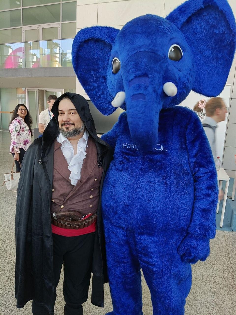 Jimmy Angelakos dressed as the character from the PostgreSQL Mistakes and How to Avoid Them book cover posing with Slonik the PostgreSQL mascot at PGConf.EU 2026