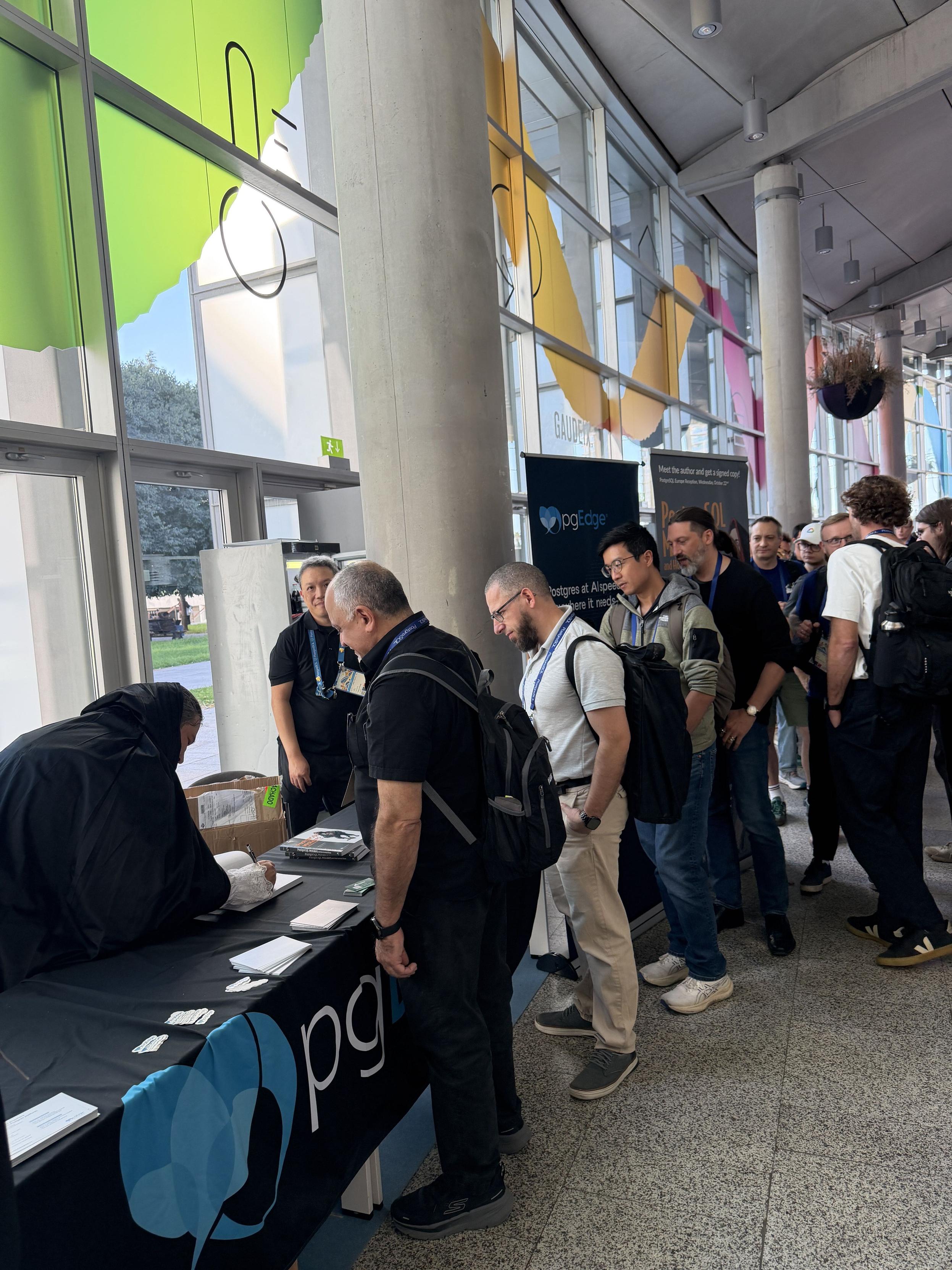 Conference attendees lined up at the pgEdge table to meet Jimmy Angelakos and get signed copies of PostgreSQL Mistakes and How to Avoid Them, with the author dressed as the character from the book cover