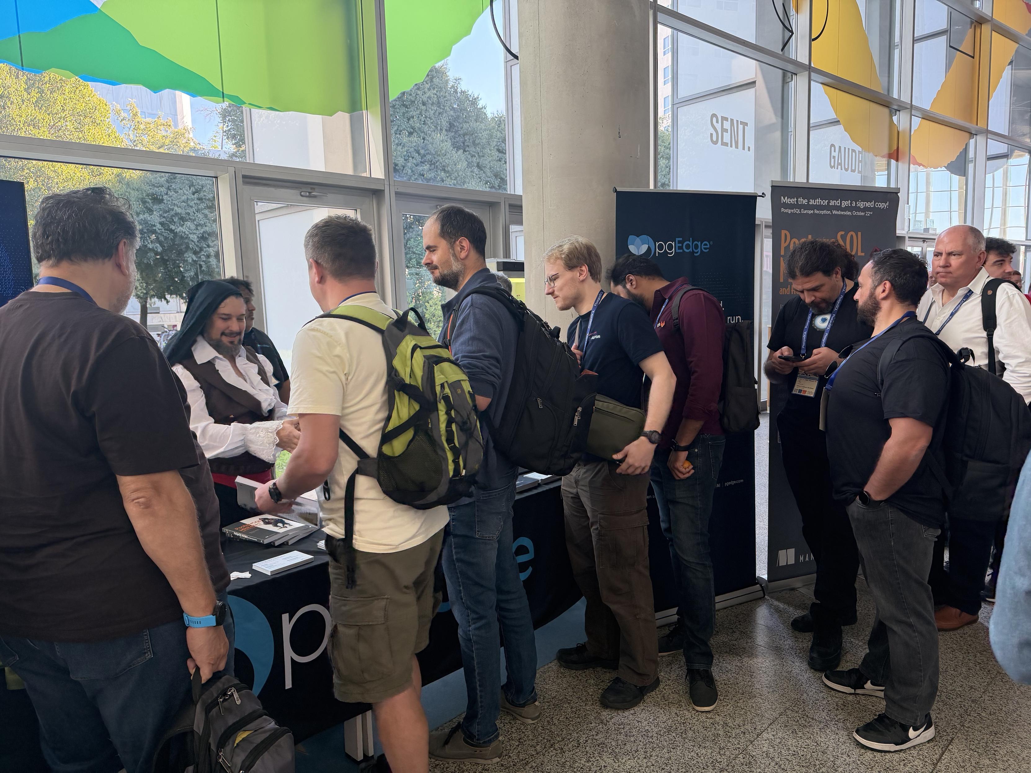 Conference attendees lined up at the pgEdge table to meet Jimmy Angelakos and get signed copies of PostgreSQL Mistakes and How to Avoid Them, with the author dressed as the character from the book cover