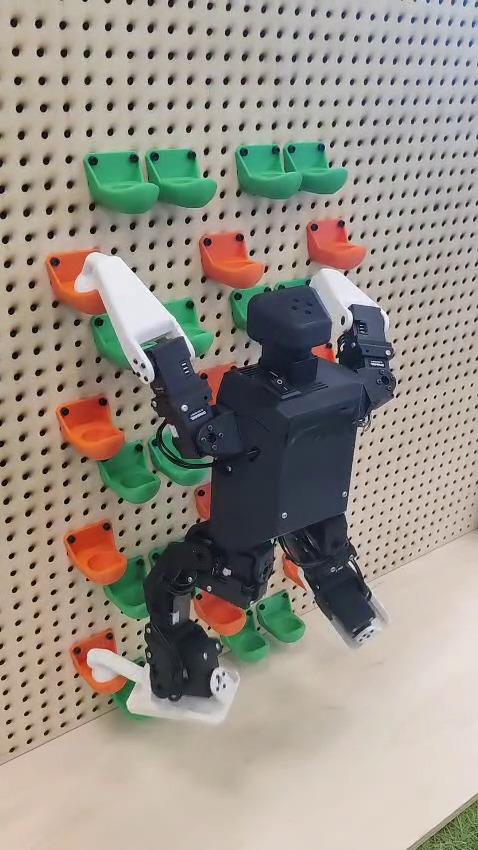 A Microban open-source humanoid robot climbing up using handholds and footholds on a climbing wall.